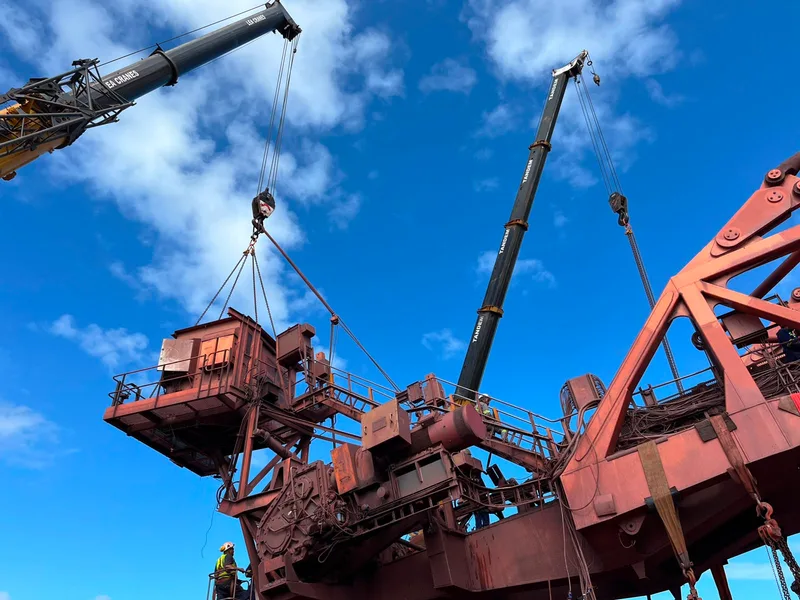 Cranes lifting heavy equipment beside a large industrial steel structure.